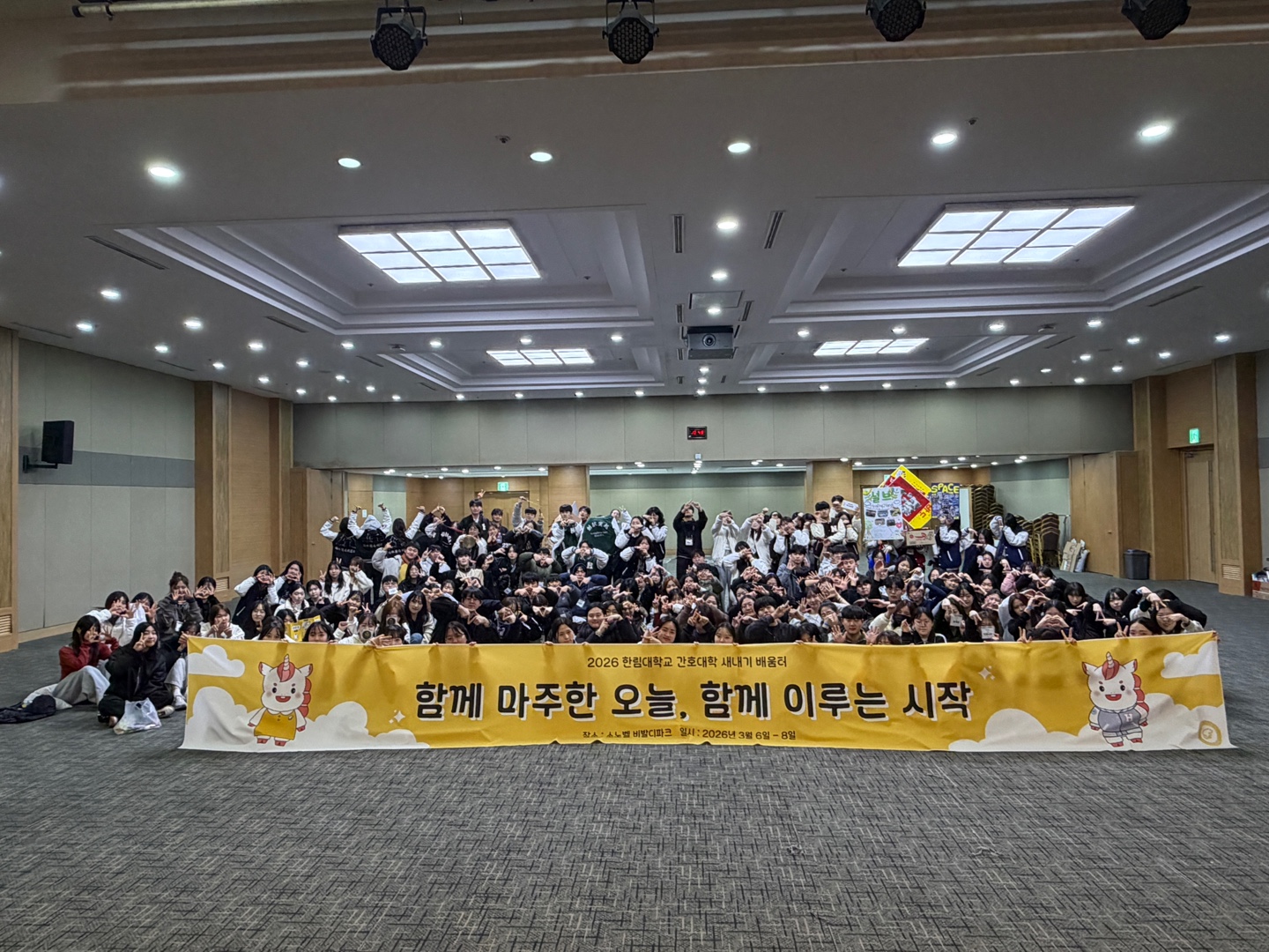 간호대학 신입생 및 재학생 약 200명이 현수막을 들고 단체사진을 찍고 있다. 현수막 내용 2026 한림대학교 간호대학 새내기 배움터 함께 마주한 오늘, 함께 이루는 시작 / 장소 소노벨 비발디 파크 / 일시 2026년 3월 6일 ~ 8일